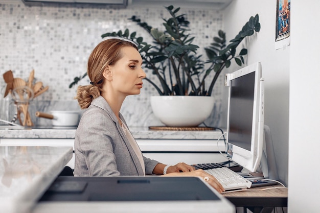 Fokussiertes hübsches ernstes Mädchen, das an ihrem Arbeitsplatz am Computer sitzt und wichtige Dinge tut. Konzept der Arbeit