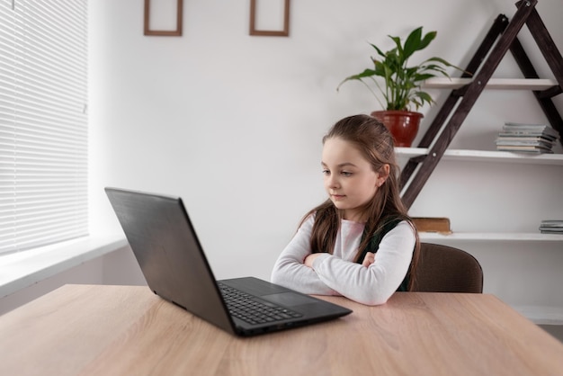 Fokussiertes Schulmädchen sitzt am Tisch und surft zu Hause mit einem Laptop im Internet Ein Kind sieht sich einen Film oder ein Video auf einem Computer an und lernt online mit einem Gadget