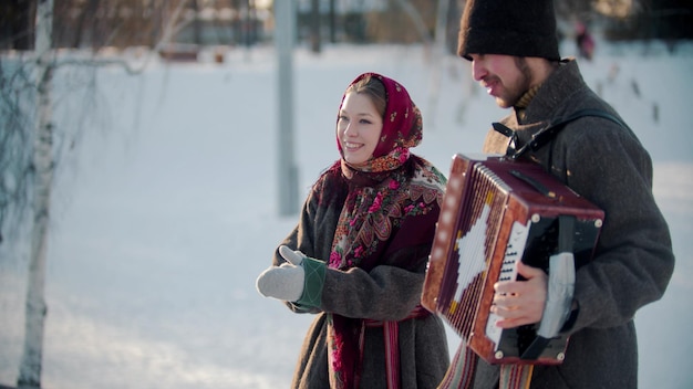 Folclore ruso hombre ruso tocando acordeón al aire libre y mujer sonriente de pie junto a él