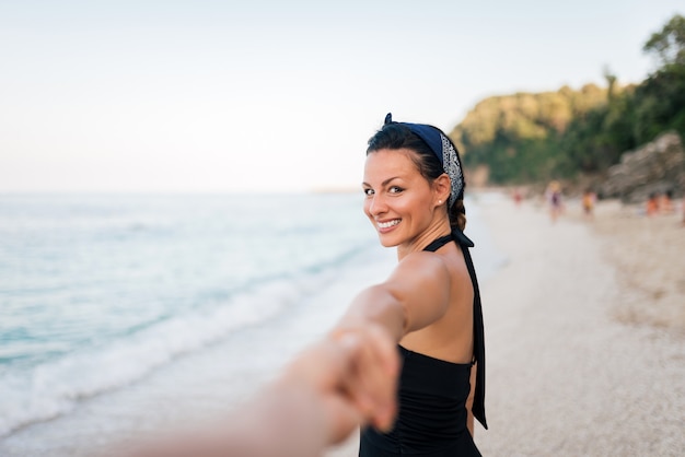 Folge mir. Glückliche junge Frau, welche die Hand des Mannes hält. Paar zu Fuß am Strand.