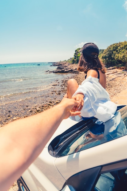 Folgen Sie mir Konzeptfrau, die auf der Motorhaube des Autos sitzt und sich am Strand ausruht