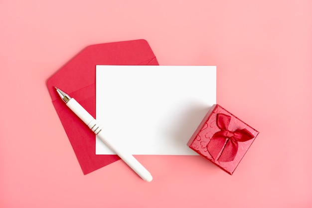 folha branca de papel para a mensagem, envelope vermelho, caixa de presente, caneta, fundo rosa. Feliz Dia dos namorados