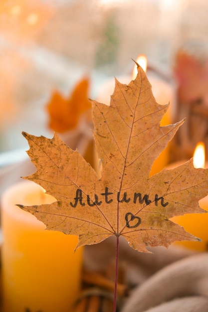 Folha de bordo de outono com texto AUTUMN no conceito de design da temporada de outono Velas no peitoril da janela clima chuvoso Atmosfera acolhedora e higiênica