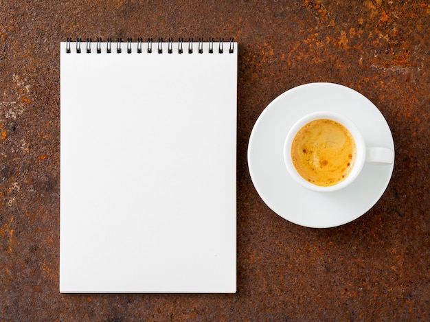 Folha de caderno em branco uma espiral e uma xícara de café na mesa de ferro velha enferrujada, vista superior.