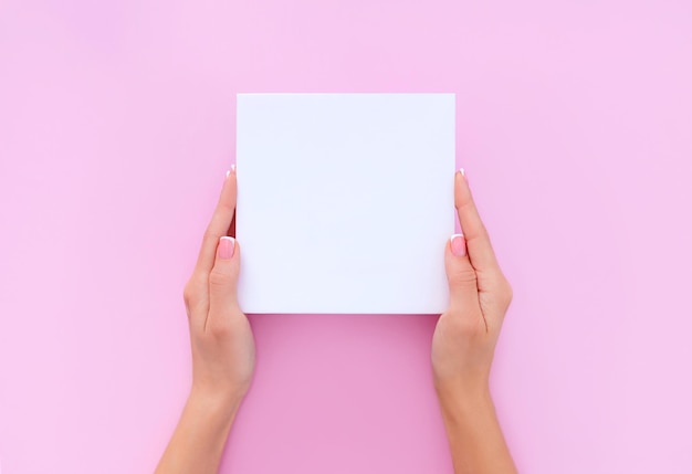 Folha de papel em branco nas mãos femininas em um fundo rosa claro