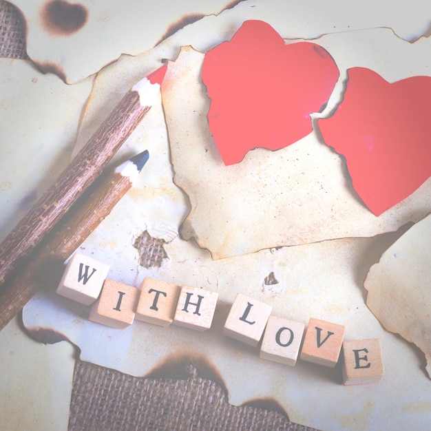 Foto folha de papel vintage velha, dois corações vermelhos, lápis de madeira e palavras com amor em cubos em pano de fundo de serapilheira efeitos de design retrô
