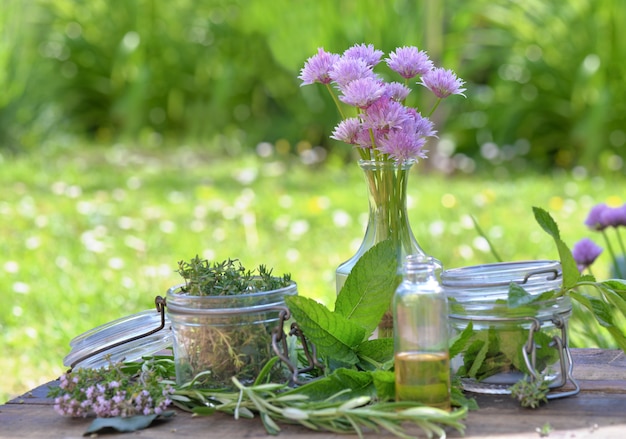 Folha de planta aromática com frasco de vidro e óleo em uma garrafa, dispostas sobre uma mesa em um jardim