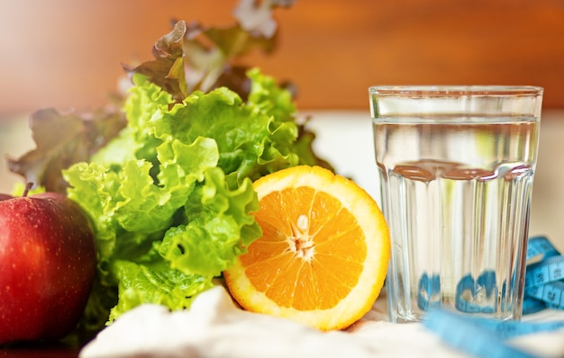 Folha de Salade. laranja, copo de água e fita métrica azul em fundo marrom, estilo de vida saudável e conceito de água potável