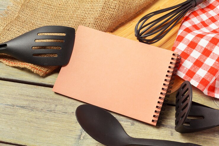 Foto folha em branco do bloco de notas aberto e utensílios de cozinha na mesa com toalha de mesa, espaço de cópia