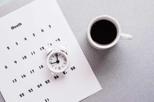 Folha em branco do calendário mensal, xícara de café e despertador em um fundo cinza. Planejamento e organização do tempo. Copie o espaço. Fechar-se