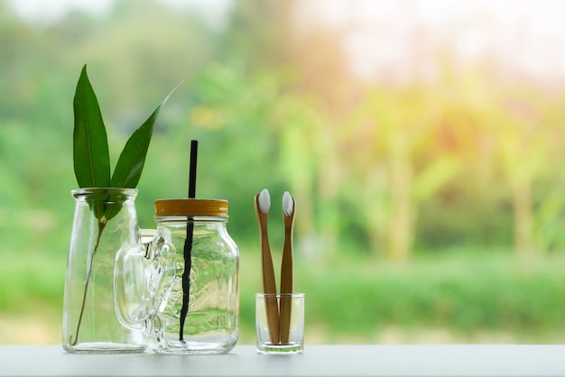 folha verde eco no frasco de vidro de água com jarro de palha vaso e escova de dentes de bambu