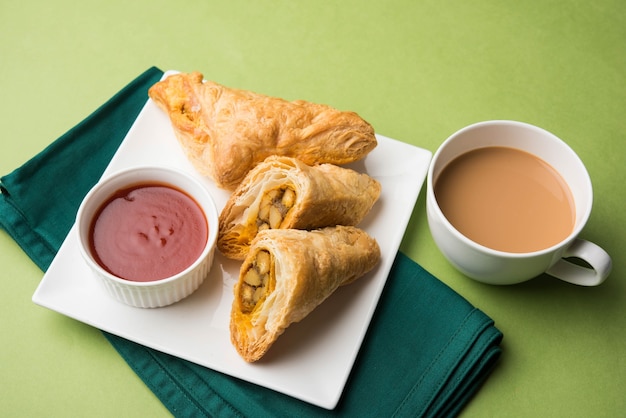 Folhada de vegetais recheados ou samosa, famoso lanche da padaria indiana, servido com ketchup de tomate e chá quente, foco seletivo