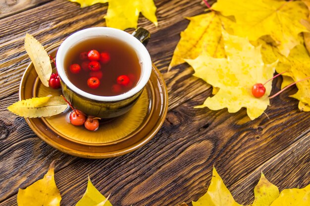 Folhas de bordo amarelas e laranja caídas no fundo da mesa de madeira castanha escura Xícara de chá