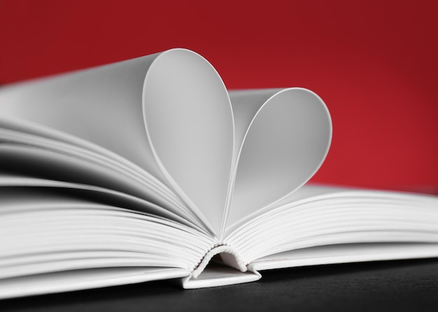 Foto folhas de livro curvadas em forma de coração em fundo vermelho desfocado