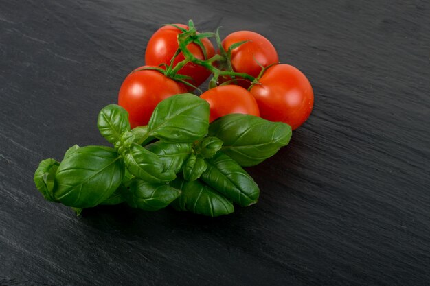 Folhas de manjericão e tomate cereja fresco fundo de pedra preta