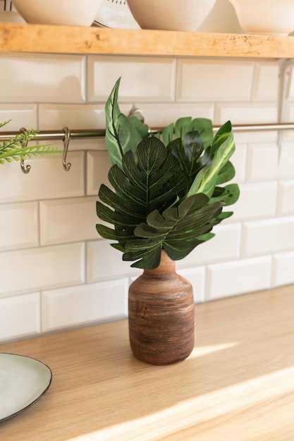 Folhas de monstera artificiais em um vaso em um fundo de estilo de cozinha escandinavo