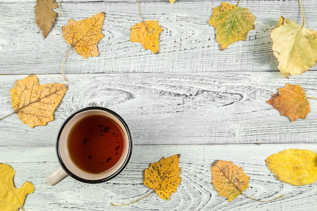 Folhas de outono amarelas, uma xícara de chá em um fundo de madeira velho
