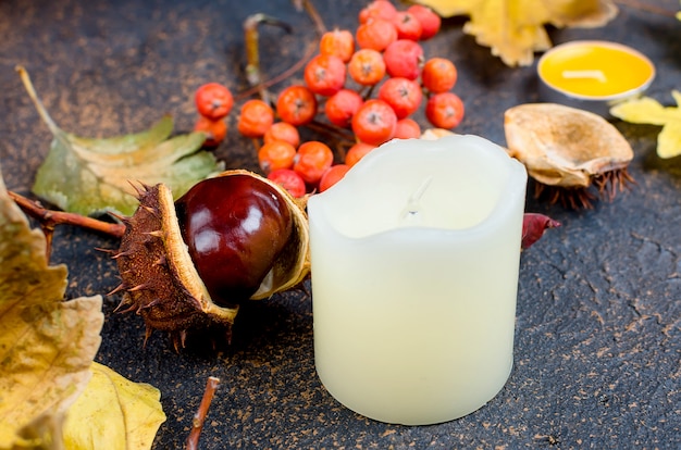 Folhas de outono, castanhas, velas em um fundo escuro