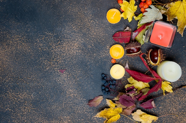 Folhas de outono, castanhas, velas em um fundo escuro