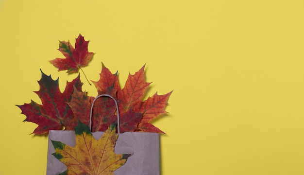 Folhas de outono coloridas em um saco de papel artesanal em um fundo amarelo. Descontos de outono e conceito de compras