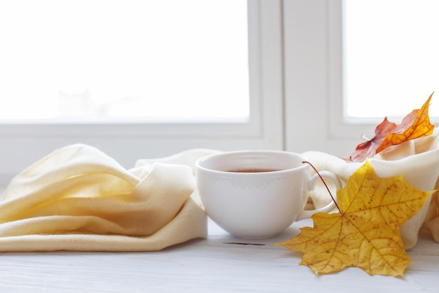 Folhas de outono com uma xícara de chá ou café ao lado de um cachecol sobre fundo de madeira com espaço de cópia