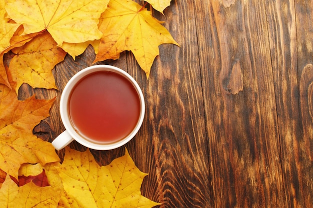 Folhas de outono com uma xícara de chá ou café em um fundo de madeira com espaço de cópia