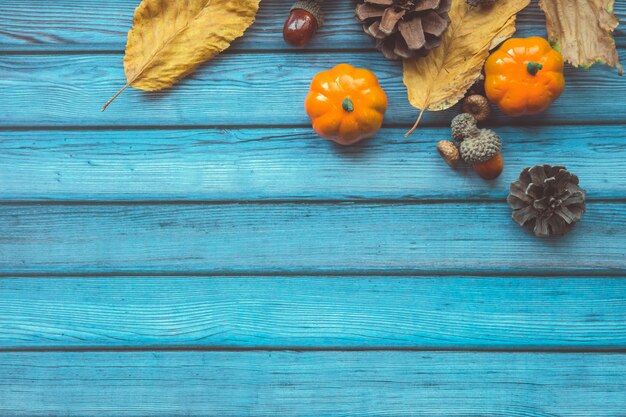 Folhas de outono, pumkins decorativos, bolotas e cones sobre fundo azul de madeira