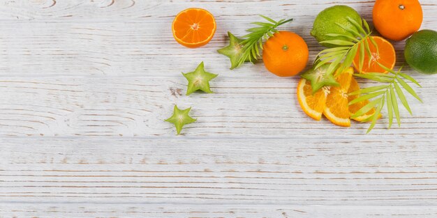 Folhas de palmeira verdes e fatias tropicais frescas de frutas na mesa de madeira branca