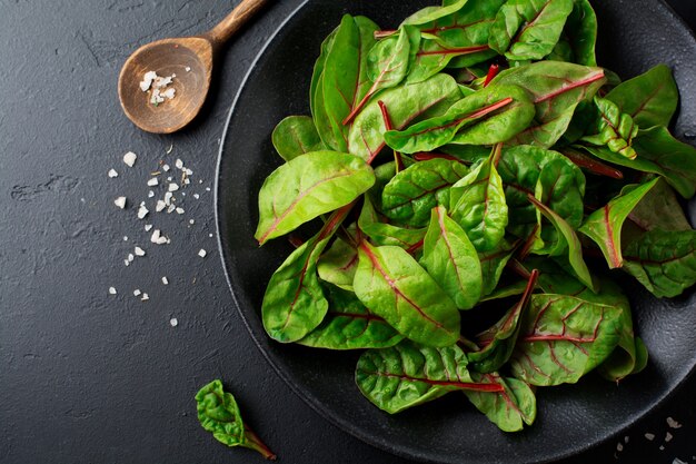 Folhas frescas de acelga para salada em um prato de cerâmica escura na mesa de concreto preto. Copie o espaço. Vista do topo.