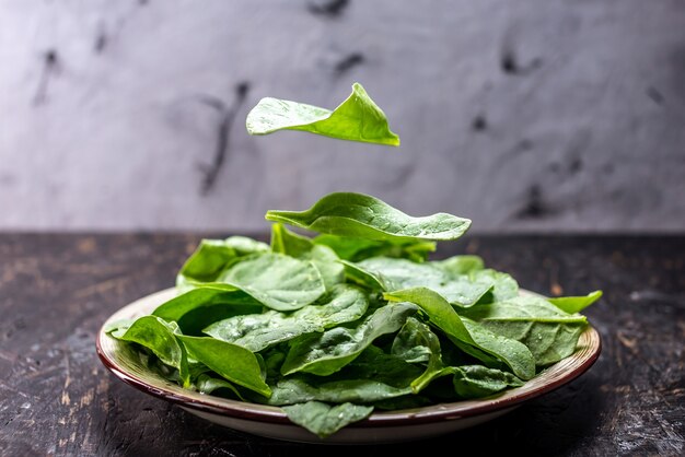 Folhas verdes de espinafre fresco em um prato no escuro