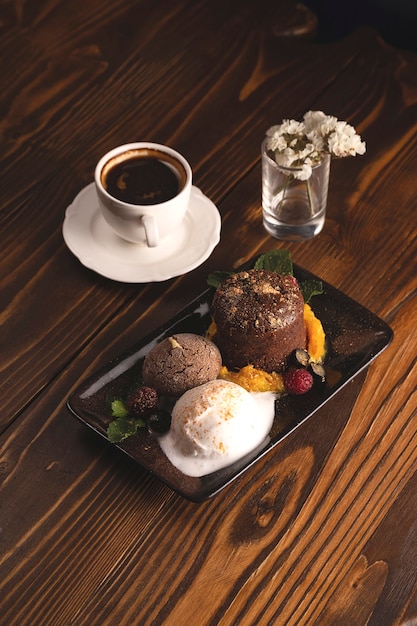 Fondant de chocolate com sorvete e frutas vermelhas em uma mesa de restaurante de madeira ao lado de uma xícara de café