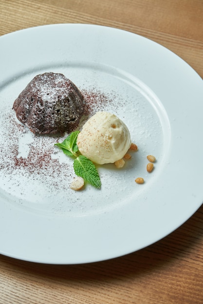 Fondant de chocolate com uma bola de sorvete de baunilha num prato branco sobre uma mesa de madeira. Sobremesa de dar água na boca no café da manhã