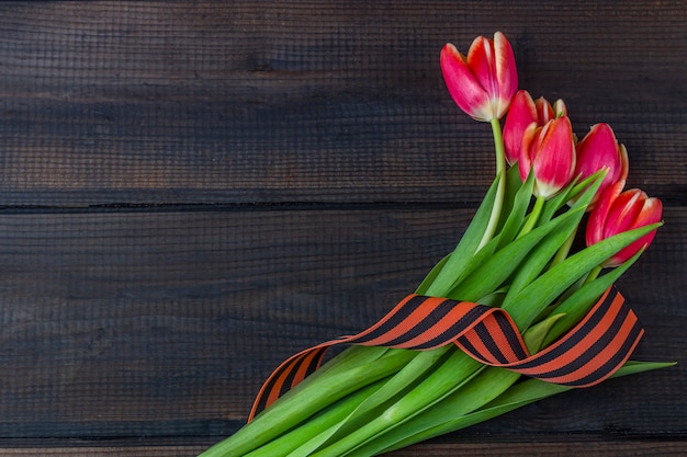 Fondo del 9 de mayo - tulipanes rojos, cinta de George en el fondo de madera. Día de la victoria o el concepto del día del defensor de la patria. Vista superior, copia espacio para texto