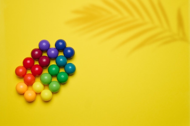 Fondo abstracto con bolas de plástico multicolores sobre un fondo amarillo un escenario para la demostración de cosméticos y productos