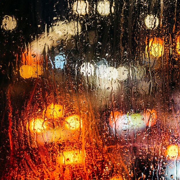 Fondo abstracto melancólico emocional con luces desenfocadas bokeh en Londres Reino Unido detrás de gotas de lluvia en el cristal de la ventana Enfoque en algunas gotas debido a la poca profundidad de campo