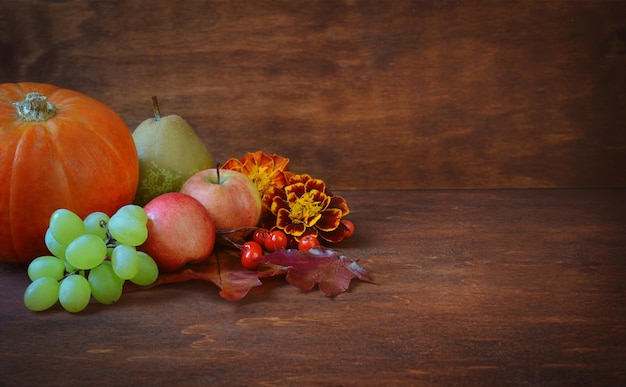 Fondo de acción de gracias con calabaza manzanas uvas y pera y flores de otoño en una mesa de madera