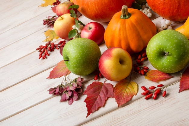 Fondo de acción de gracias con calabazas, calabaza naranja, hojas de otoño, manzanas rojas y verdes en la mesa de madera blanca