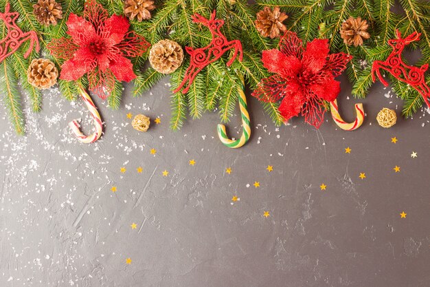 Fondo con adornos navideños tradicionales: flor roja, venado, caña de caramelo. fondo negro con ramas de abeto y conos. Copie el espacio.