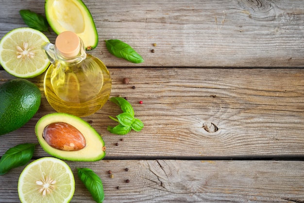 Fondo de alimentos con aguacate, lima, aceite de oliva y albahaca sobre tablas viejas desgastadas. Vista superior, espacio para texto.