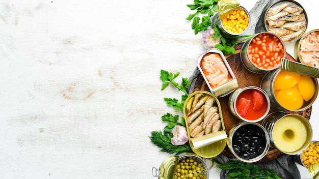 Fondo de alimentos en latas Verduras enlatadas frijoles pescado y frutas sobre un fondo de madera blanca Vista superior