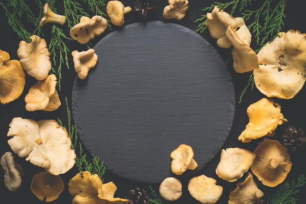 Fondo de alimentos con rebozuelos de setas alrededor de una tabla de cortar de pizarra.