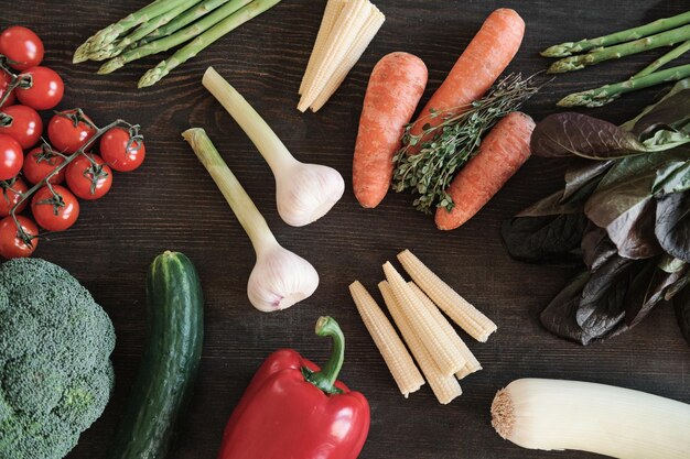 Fondo de alimentos saludables ajos zanahorias pepino espárragos callos tomates pimiento y verduras en la mesa de madera oscura