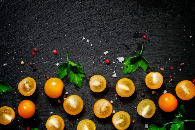 Fondo de alimentos tomate cherry amarillo mitades sal especias en una vista superior de fondo oscuro