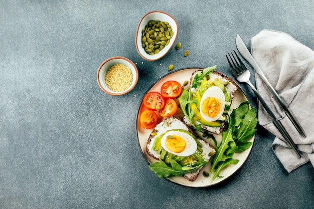 Fondo de alimentos. Vista superior de tostadas de aguacate con requesón, huevos, rúcula y tomates en la mesa. Desayuno saludable, merienda. Copia espacio