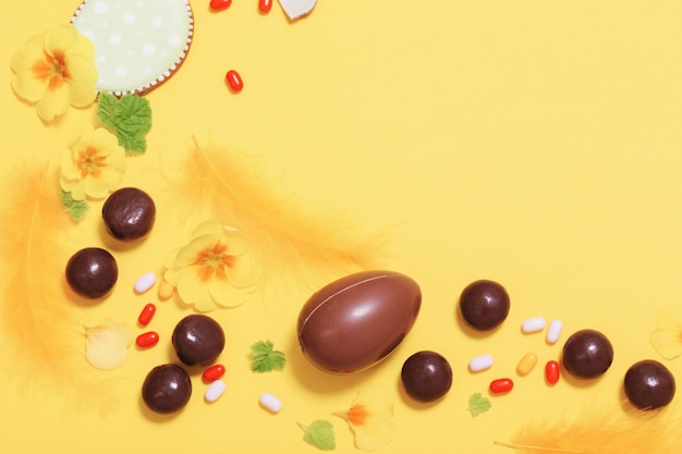 Fondo amarillo de Pascua con huevos de chocolate, dulces y flores de primavera