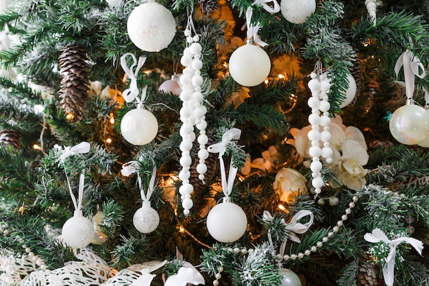 Fondo de ambiente de vacaciones de invierno. Primer plano de abeto bellamente decorado con adornos blancos modernos, barbas y guirnalda brillante. Magia de navidad y año nuevo en casa