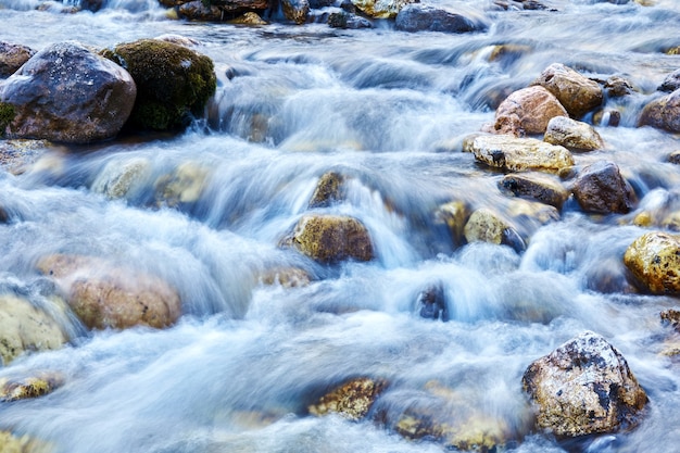 Foto fondo: un arroyo de montaña en un canal rocoso, el agua se ve borrosa en movimiento