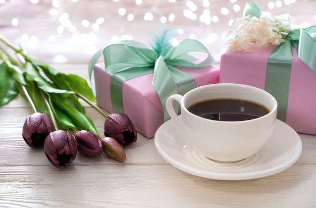 Fondo atmosférico festivo con una taza de café, flores y envases de regalo en el fondo de