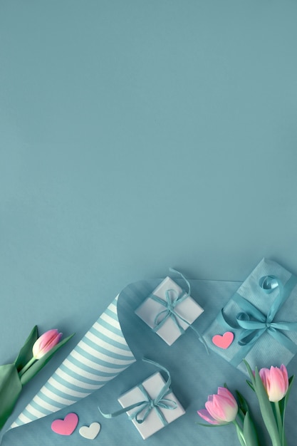 Fondo azul con tulipanes rosados, papel de regalo a rayas y cajas de regalo,