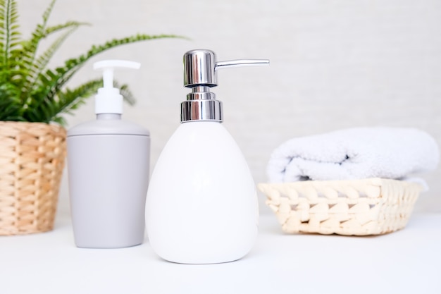 Fondo de baño, accesorios de baño para el cuidado de las manos y el cuerpo, dispensador de jabón líquido y toallas contra un fondo claro.